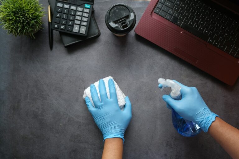 Petugas kebersihan kantor memakai sarung tangan biru membersihkan meja